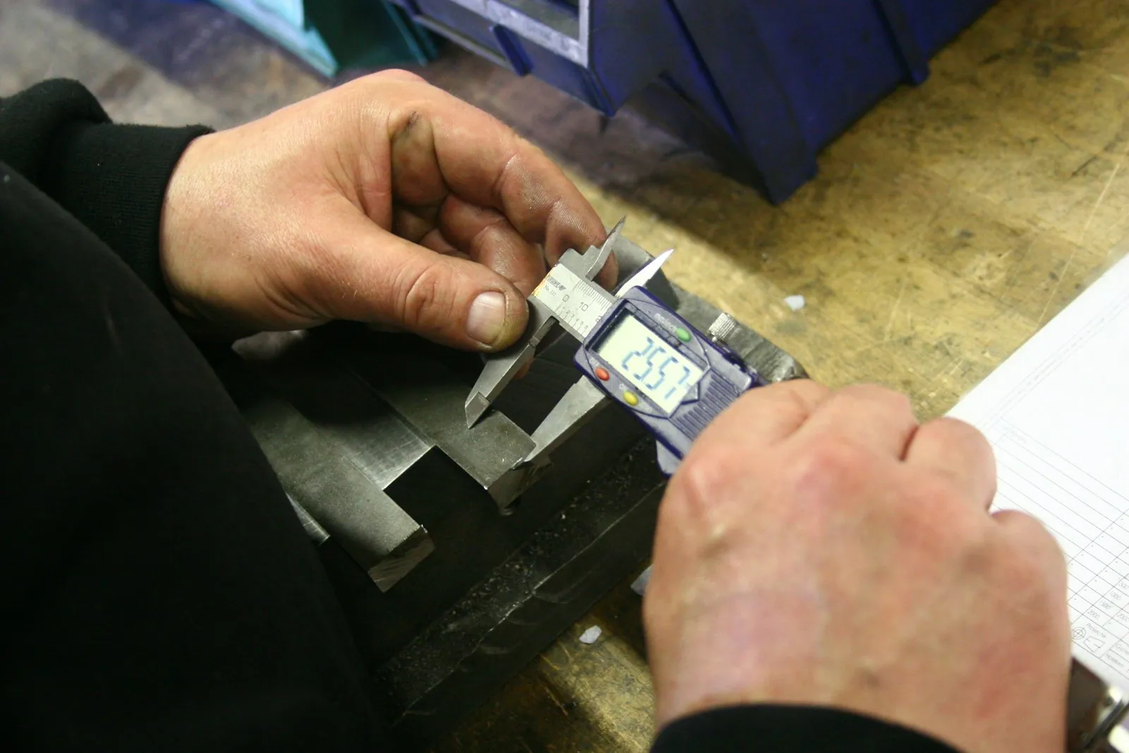 Hands measuring a machined metal part with a digital vernier caliper