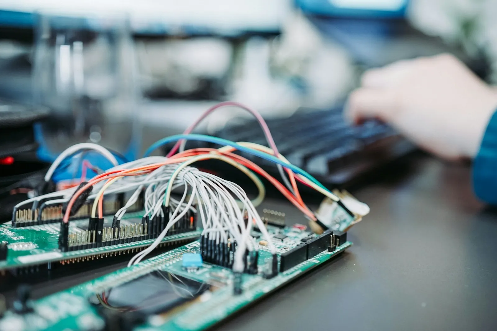 Engineer typing at a keyboard beside a development board wired with jumper leads