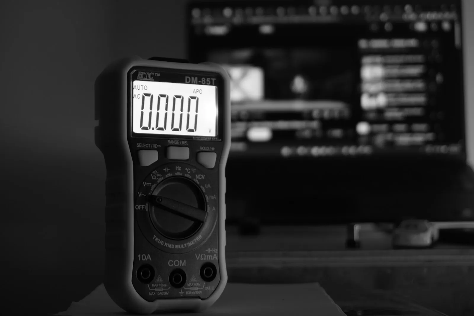 Digital multimeter reading zero volts in front of a computer screen
