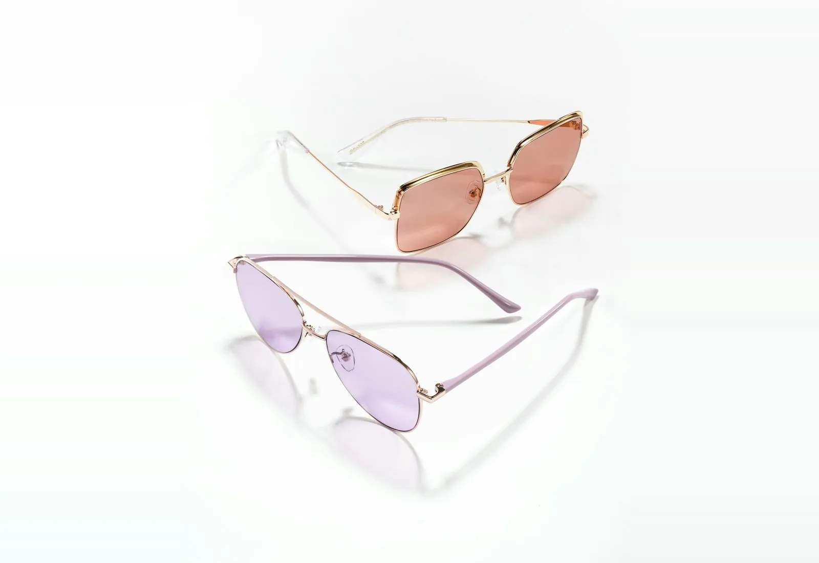 Two pairs of glasses with pink and lilac tinted lenses on a white surface