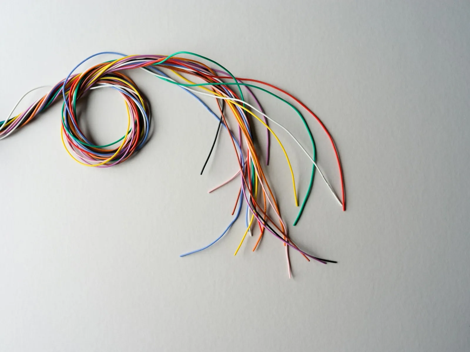 Bundle of colour-coded insulated wires coiled on a pale grey surface
